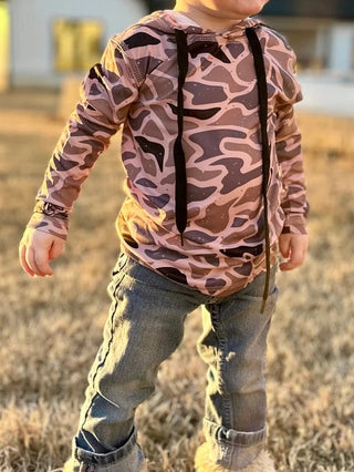 Child in brown camouflage shirt and jeans standing in a field with a house in the background